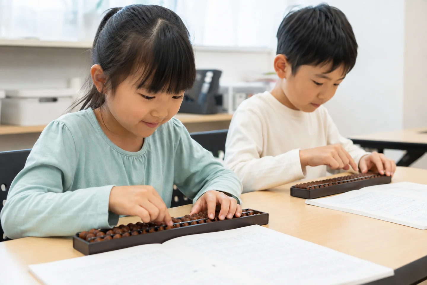 机に並んで、そろばんの珠を動かす2人の子ども