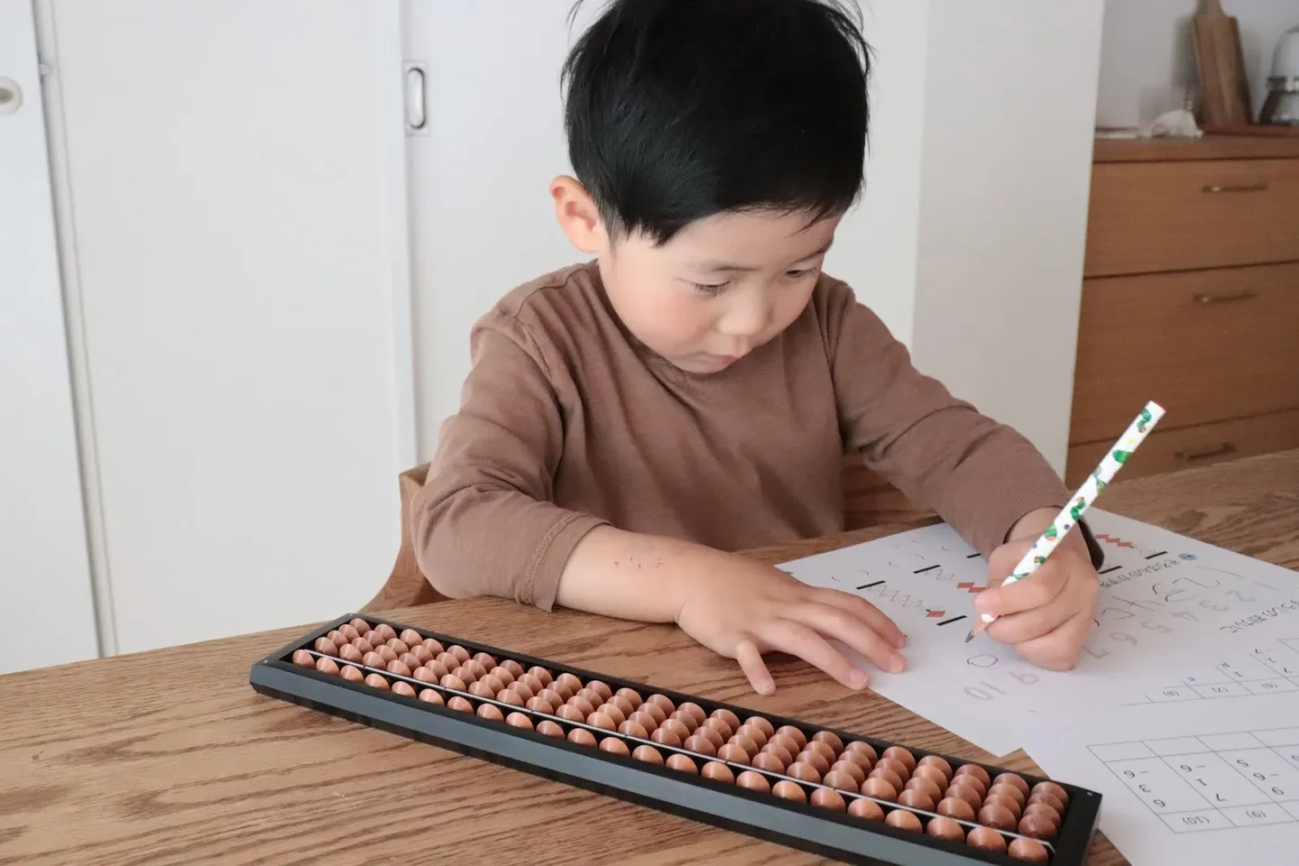 そろばんを机に置き、鉛筆で問題の答えを書く子ども
